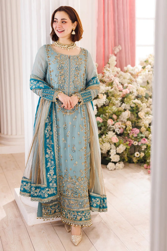 Woman in a light blue embroidered traditional outfit standing in a decorated room with flowers.