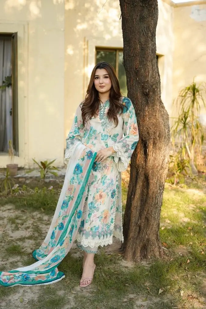 A woman wearing a traditional three-piece floral salwar kameez suit in white, teal, and pink, standing outdoors next to a tree.