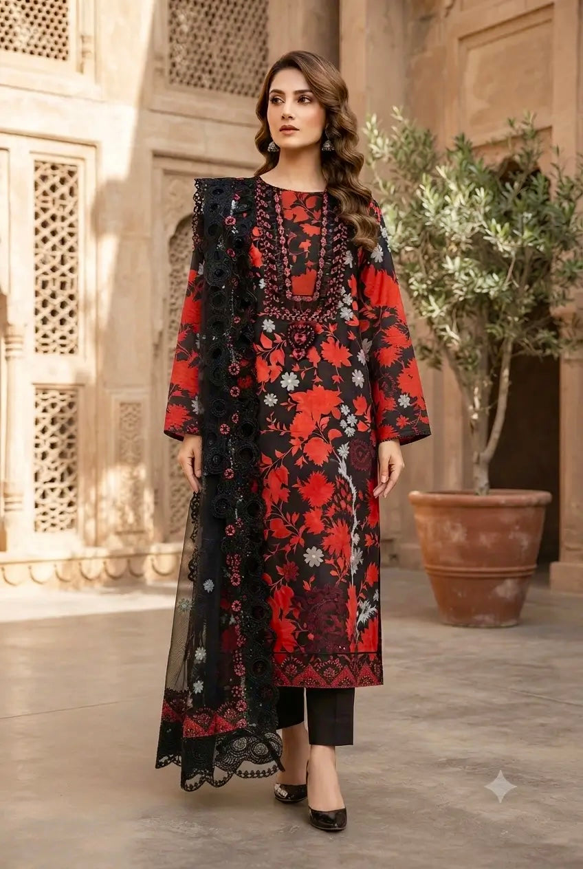 A woman models a traditional three-piece salwar kameez suit in a courtyard setting. The set features a red and black floral print kurta with black embroidery, black trousers, and a matching black sheer dupatta.