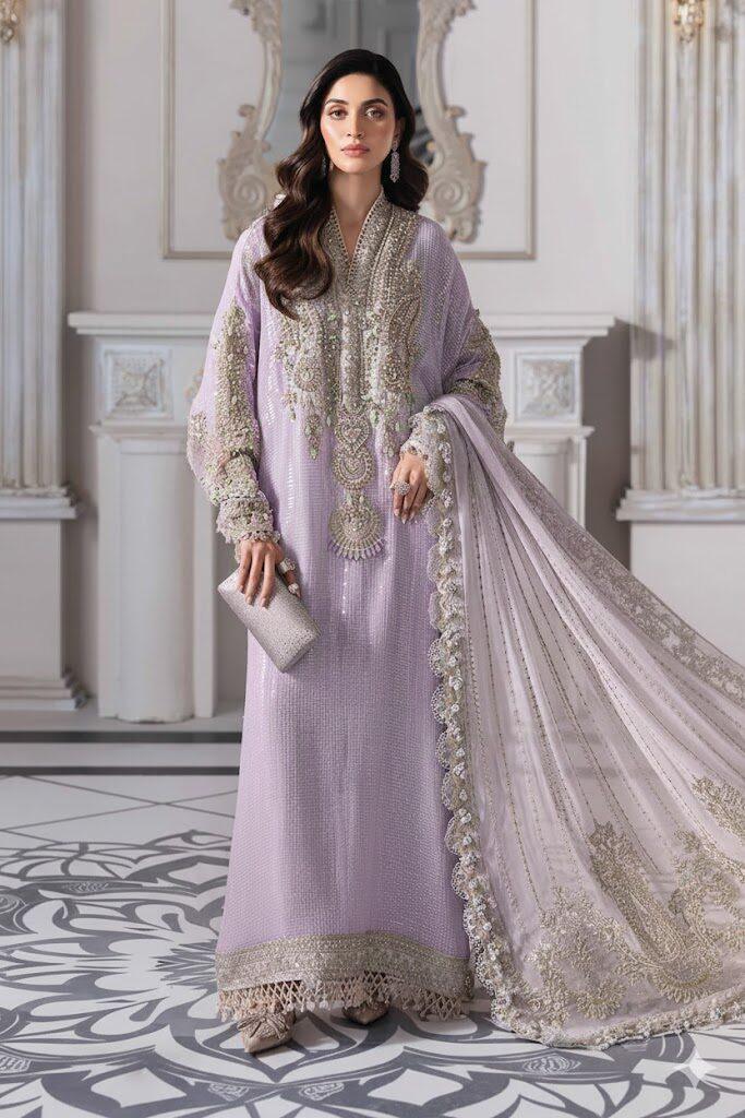 Model wearing Maria B Lalic hand-embellished lilac chiffon long shirt dress with embroidered dupatta and raw silk trousers. Shop now at Pakiclothing.