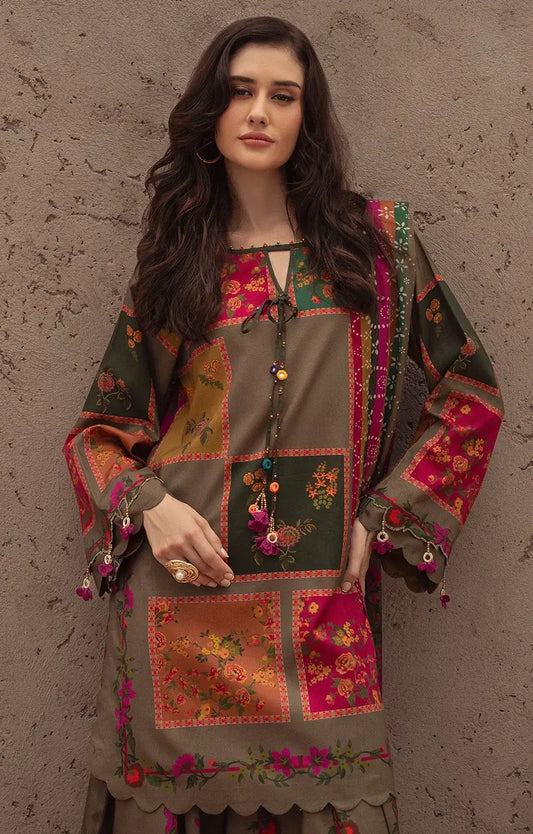 A woman models a traditional patchwork embroidered kurta in olive green, pink, and orange, set against a textured brown stucco wall.
