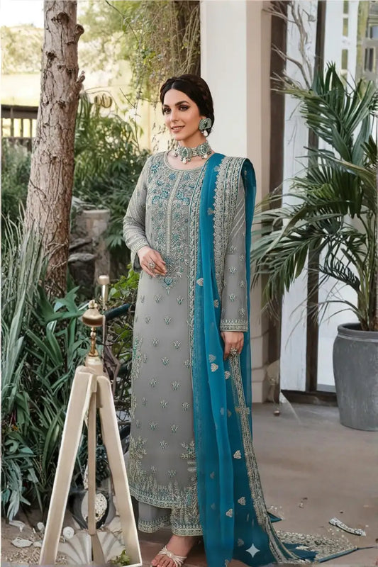Woman in a gray and blue traditional outfit standing outdoors with plants and decor.