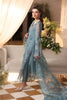 Woman in a teal embroidered outfit standing in an elegant indoor setting.